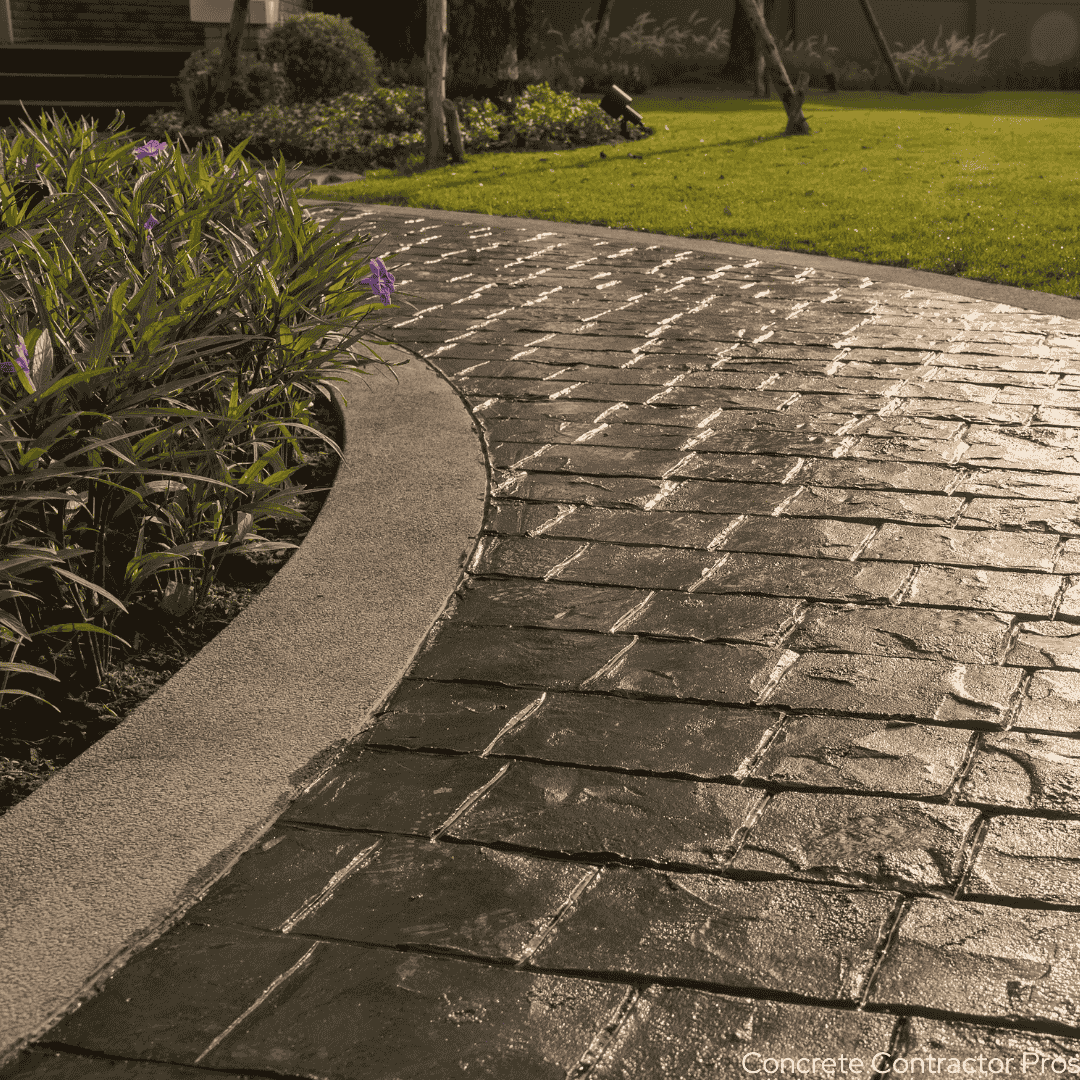 Curved sidewalk that is stamped concrete with plants to the left and a concrete trim on the edges.
