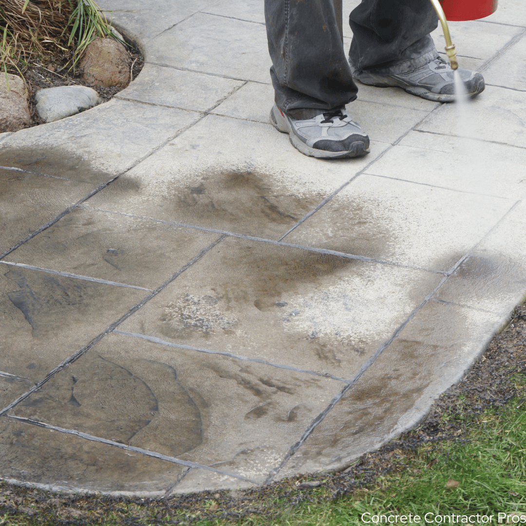 Worker standing on a stamped concrete sidewalk spraying it with a sealer.